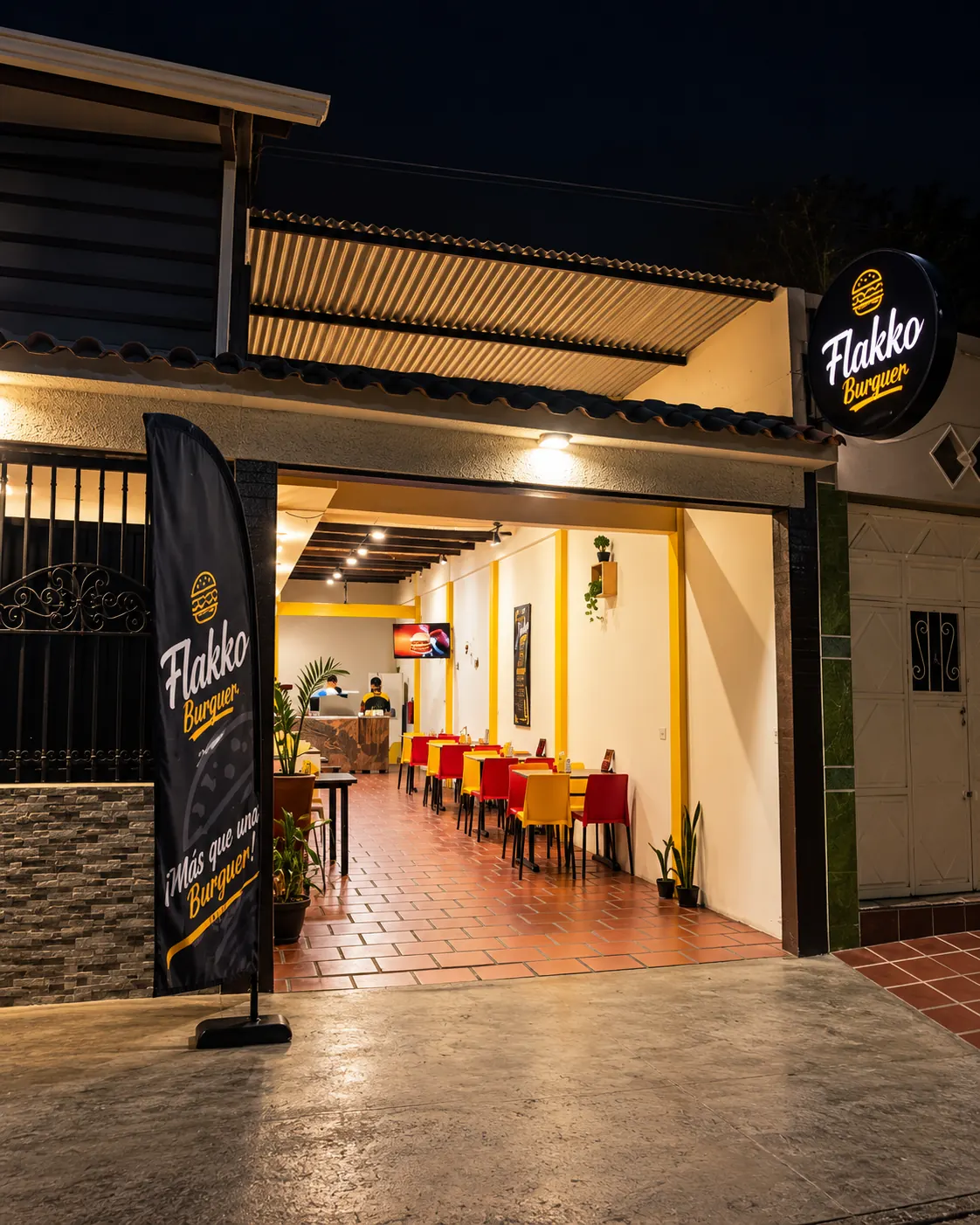 Entrada de Flakko Burguer en Rubio de noche, con el salón de mesas rojas y amarillas al fondo